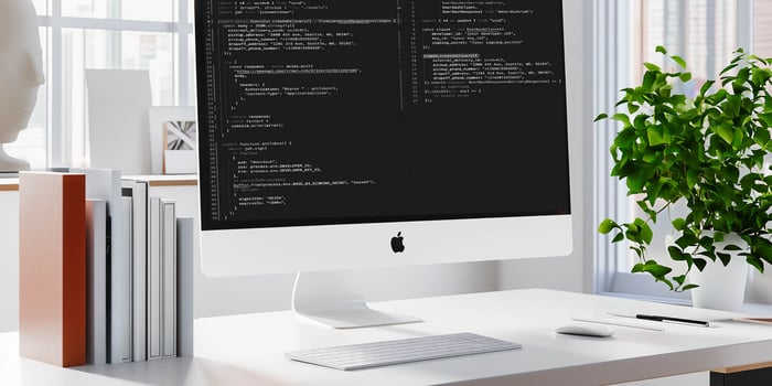 A PC with code on screen standing on a white neatly organised desk