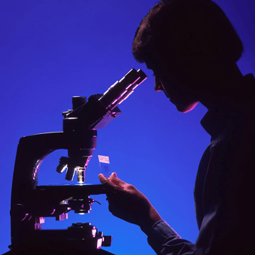 profile of a young man looking through a microscope with blue background