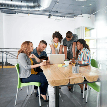 A group of working professionals gathered around a laptop placed on a table 